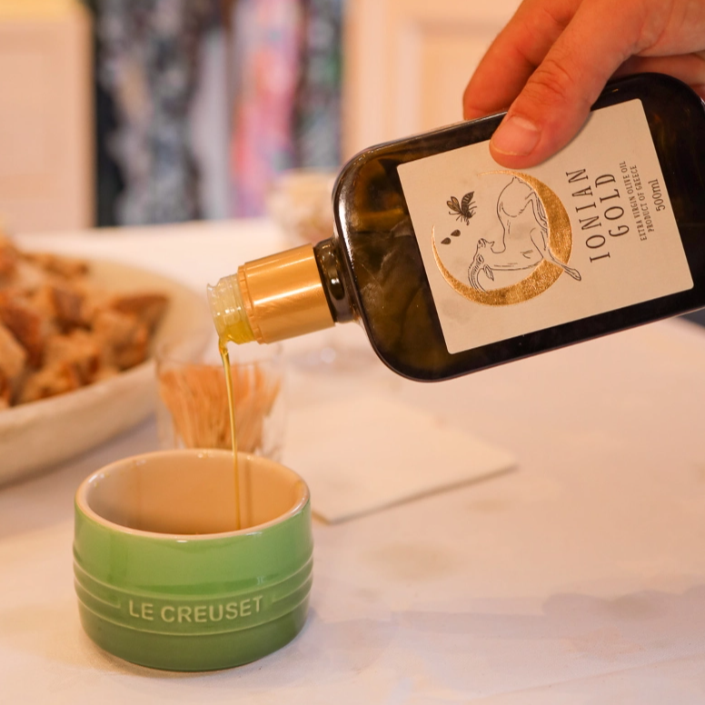 Person pouring Ionian Gold olive oil into a green bowl.