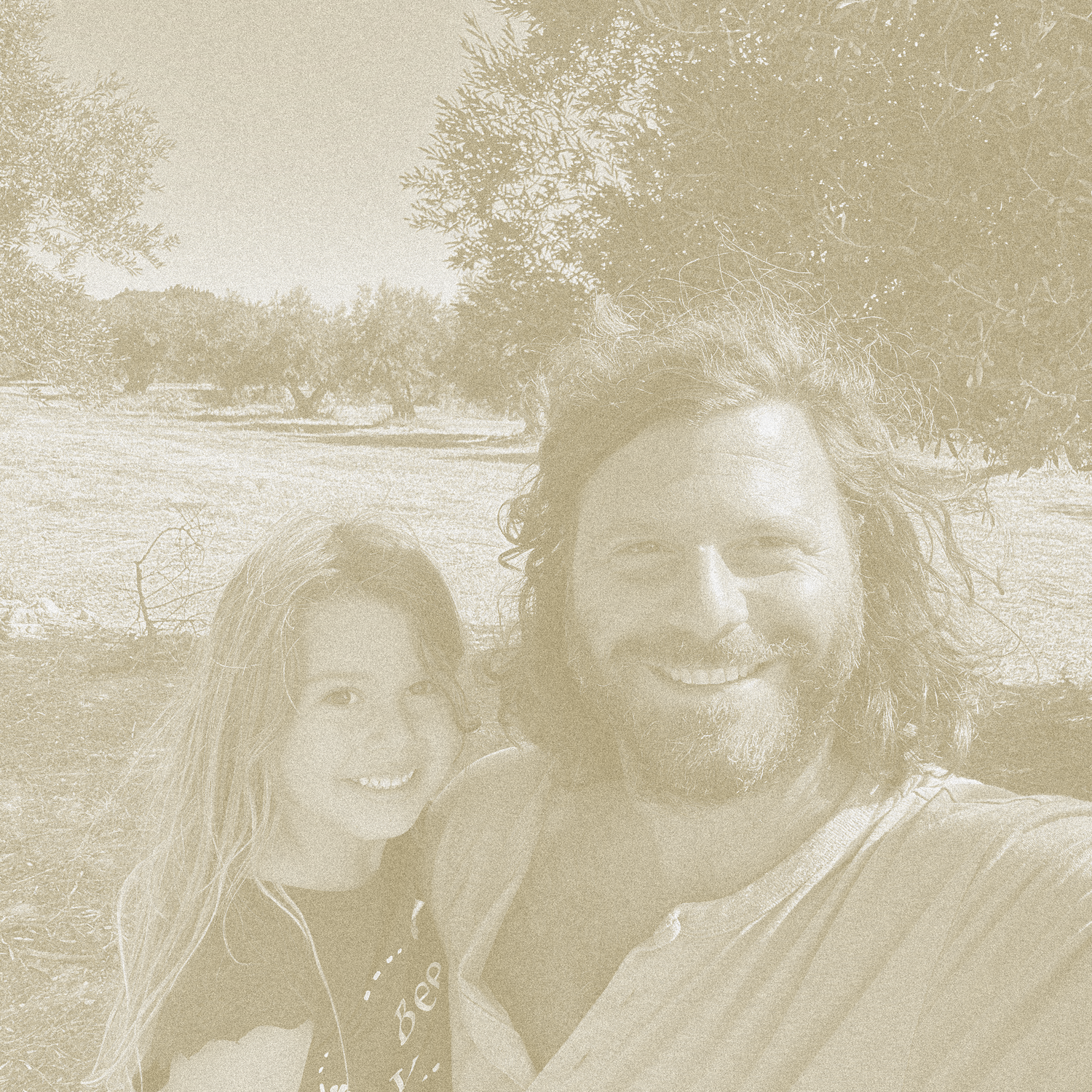 Two people standing outdoors with trees and olive groves in the background